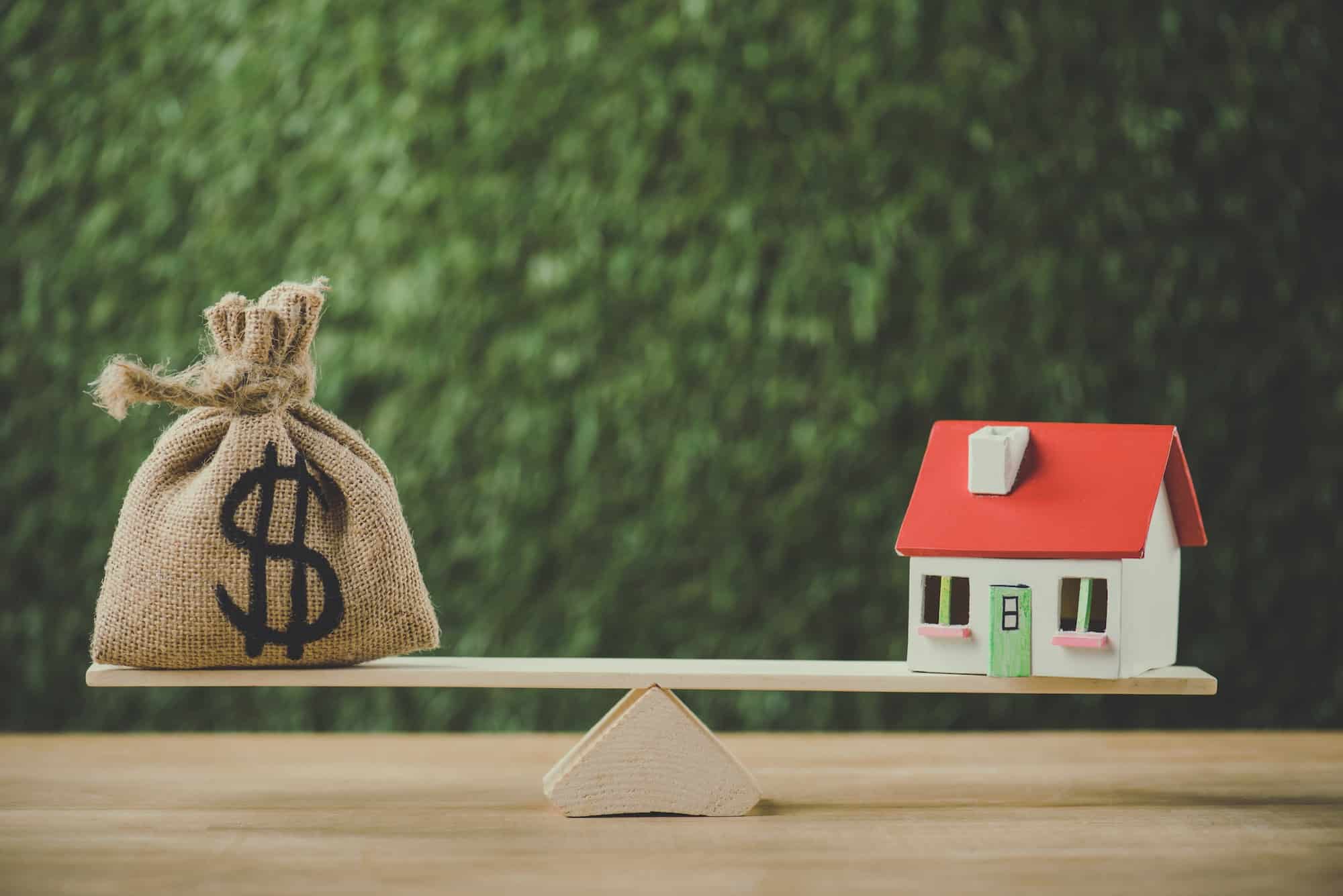 money bag with dollar symbol and house model balancing on swing on green background
